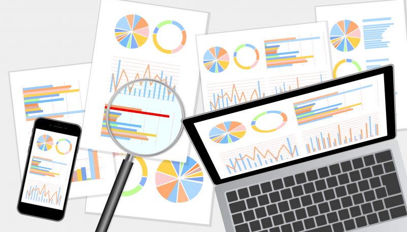 グラフ資料をモニターに表示したノートパソコン・スマホ・虫眼鏡
